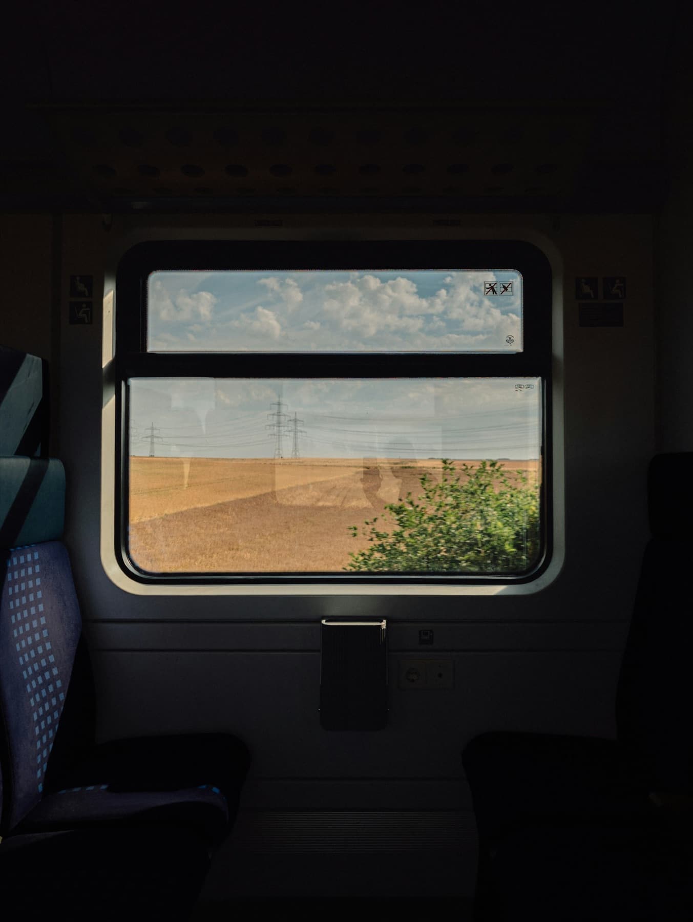 Empty train compartment with a rounded window over a harvested wheat field under cumulus clouds