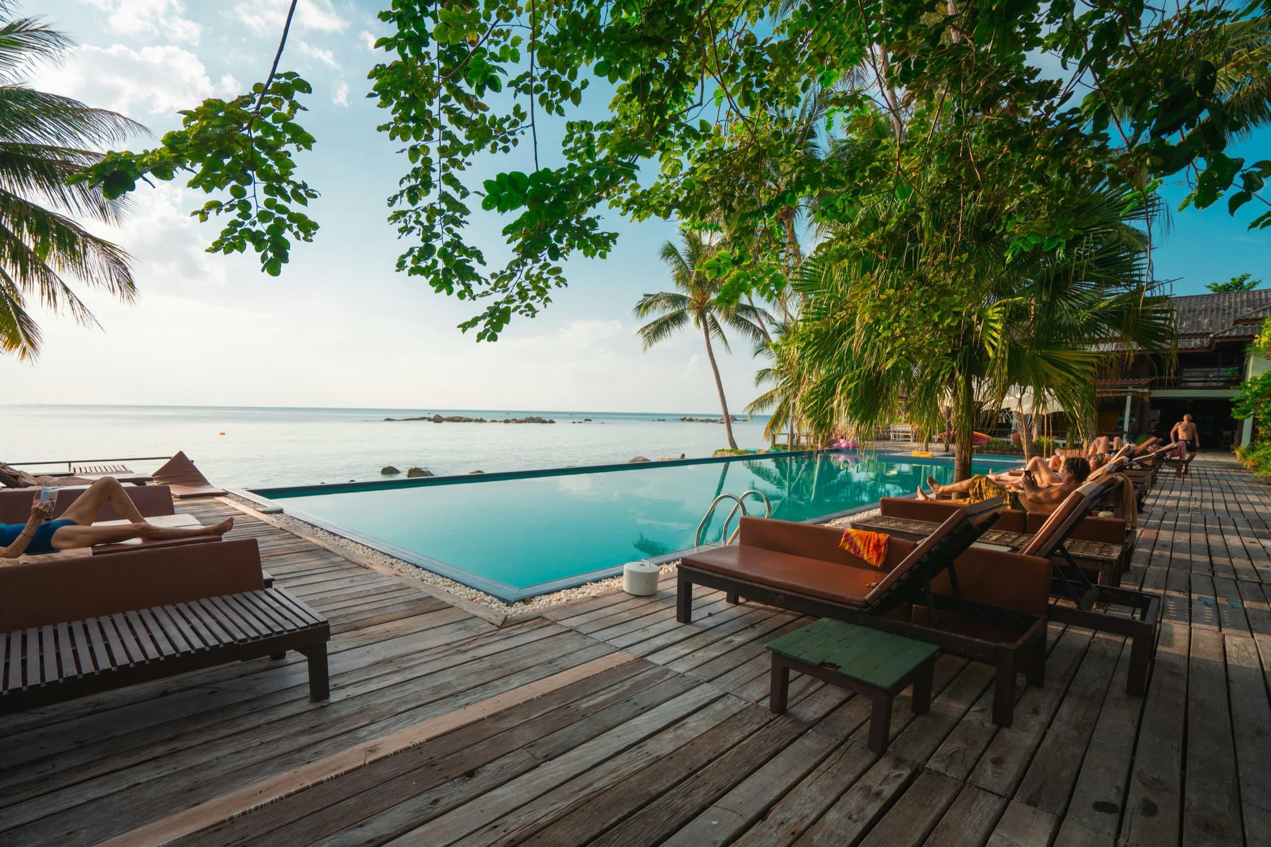 Beachfront luxury resort hotel with an oceanview pool deck, palm trees, and wooden sun loungers
