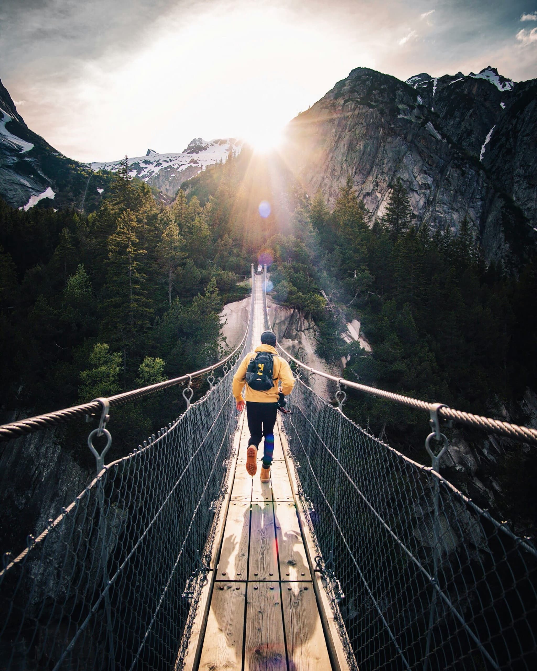 Traveler running across a mountain suspension bridge at sunrise on a guided adventure tour