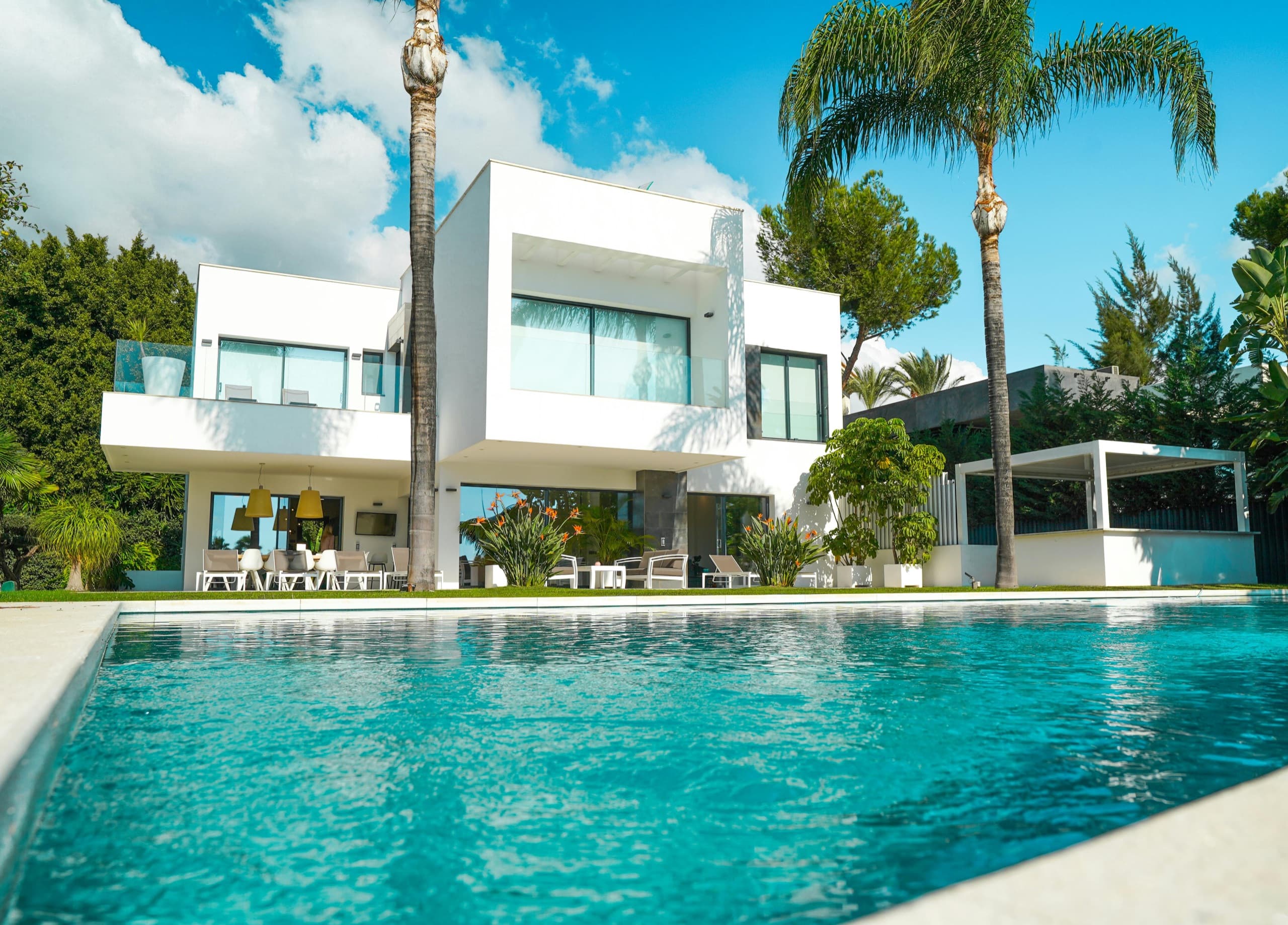Modern white private villa with a large outdoor pool and palm trees, a condo-style weekly vacation stay