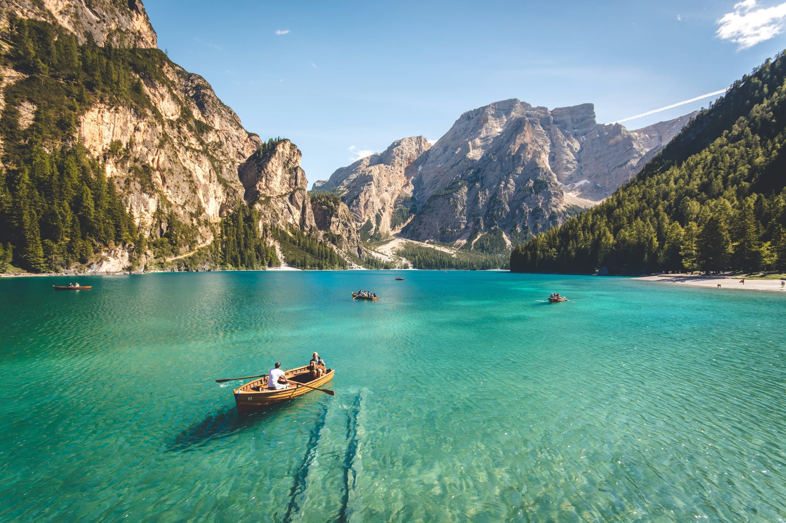 Travelers rowing wooden boats across a turquoise alpine lake beneath jagged mountain peaks