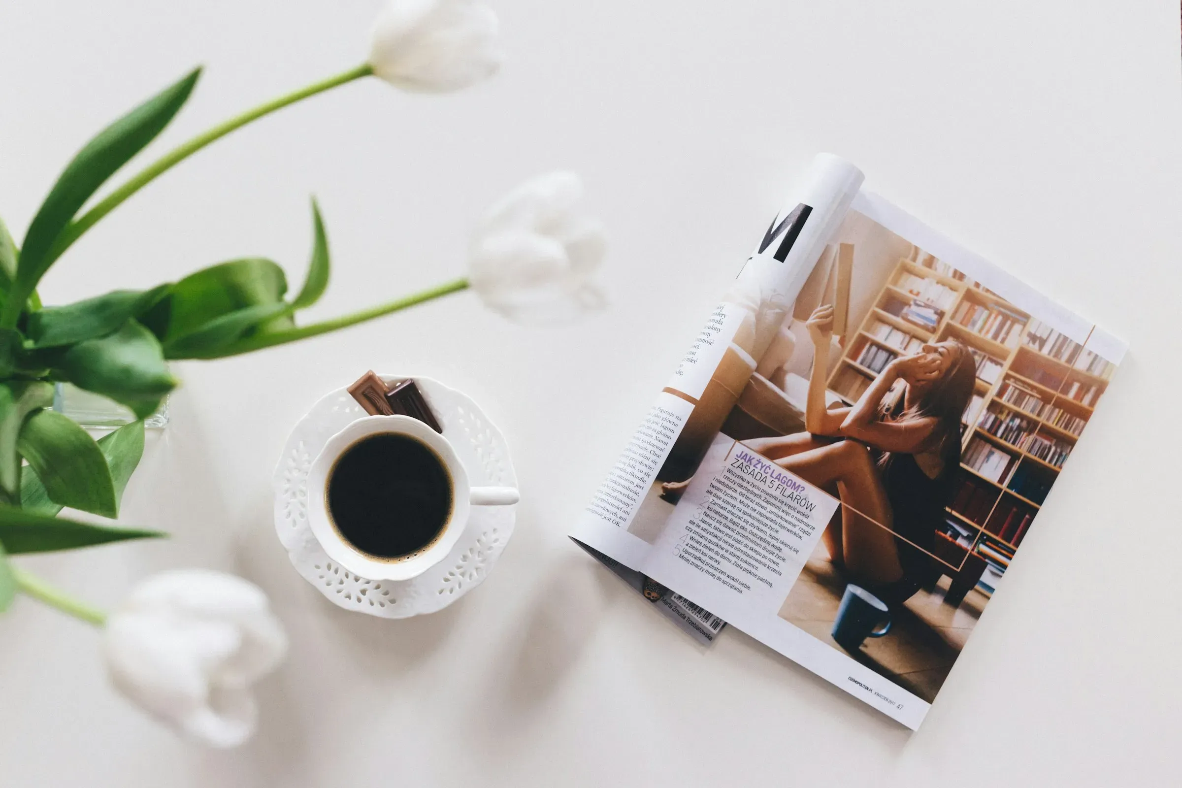 An open magazine beside a cup of black coffee and white tulips
