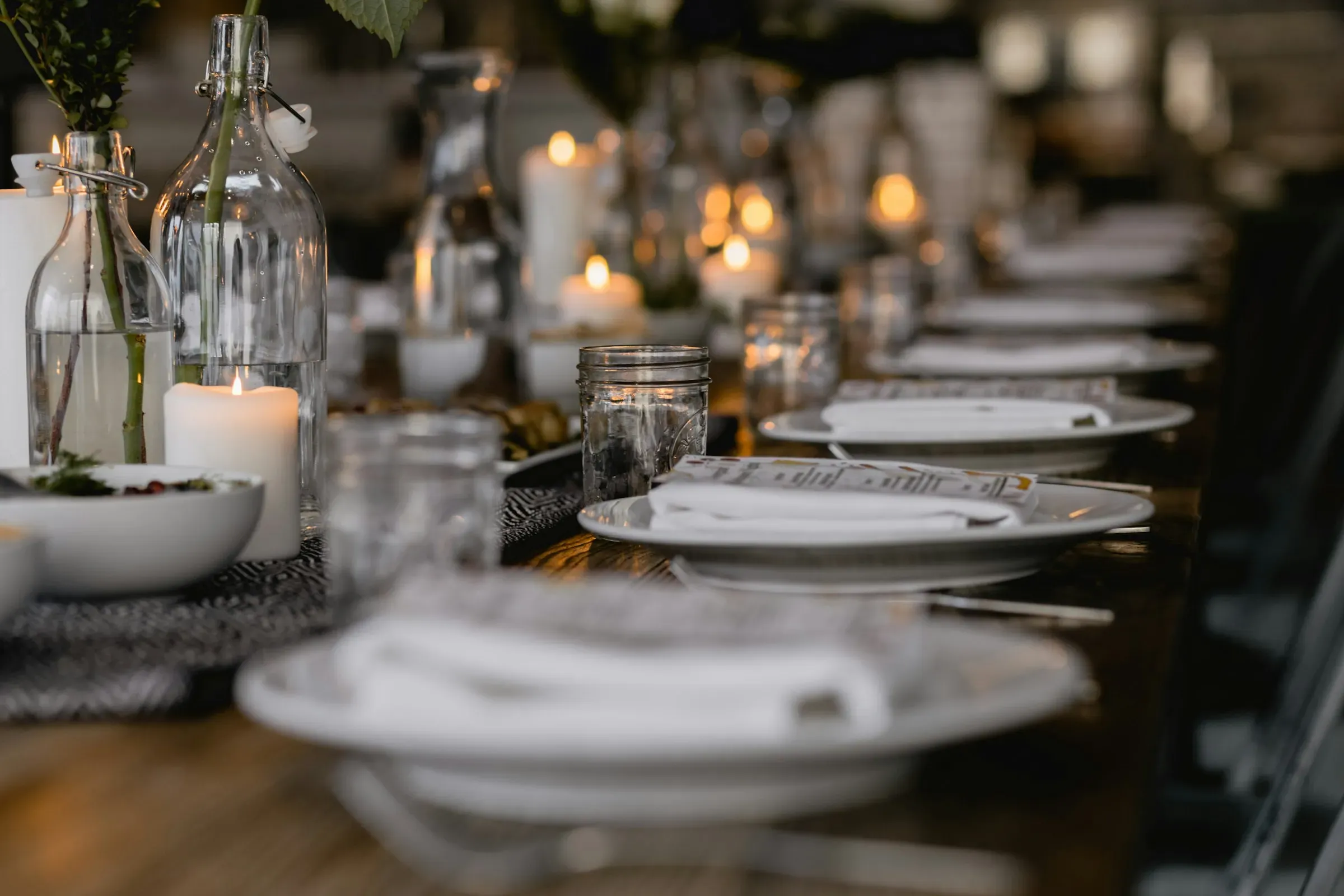 A long dinner table set with candles, glasses and white plates