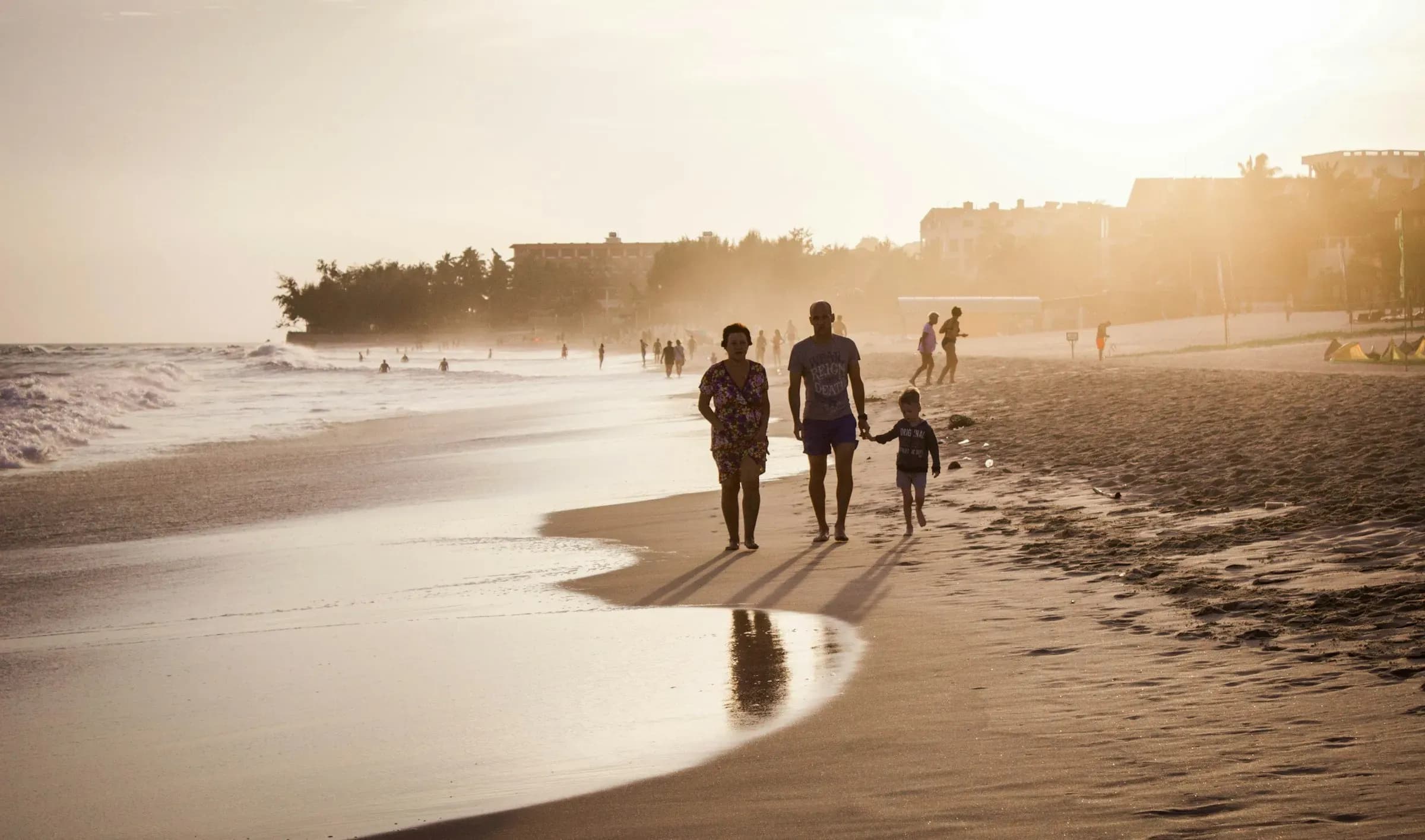 A family walking along the water's edge on a beach in golden light