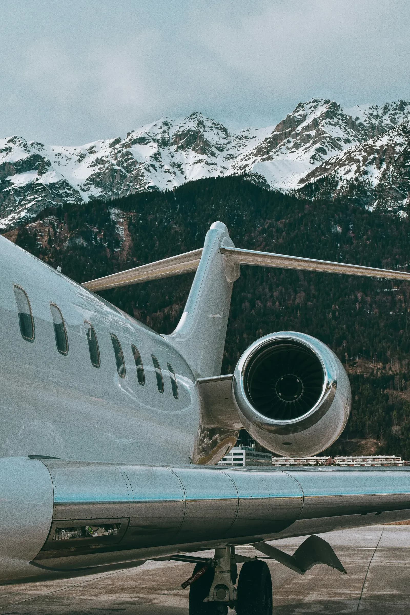 The engine and wing of a private jet with snowy mountains behind