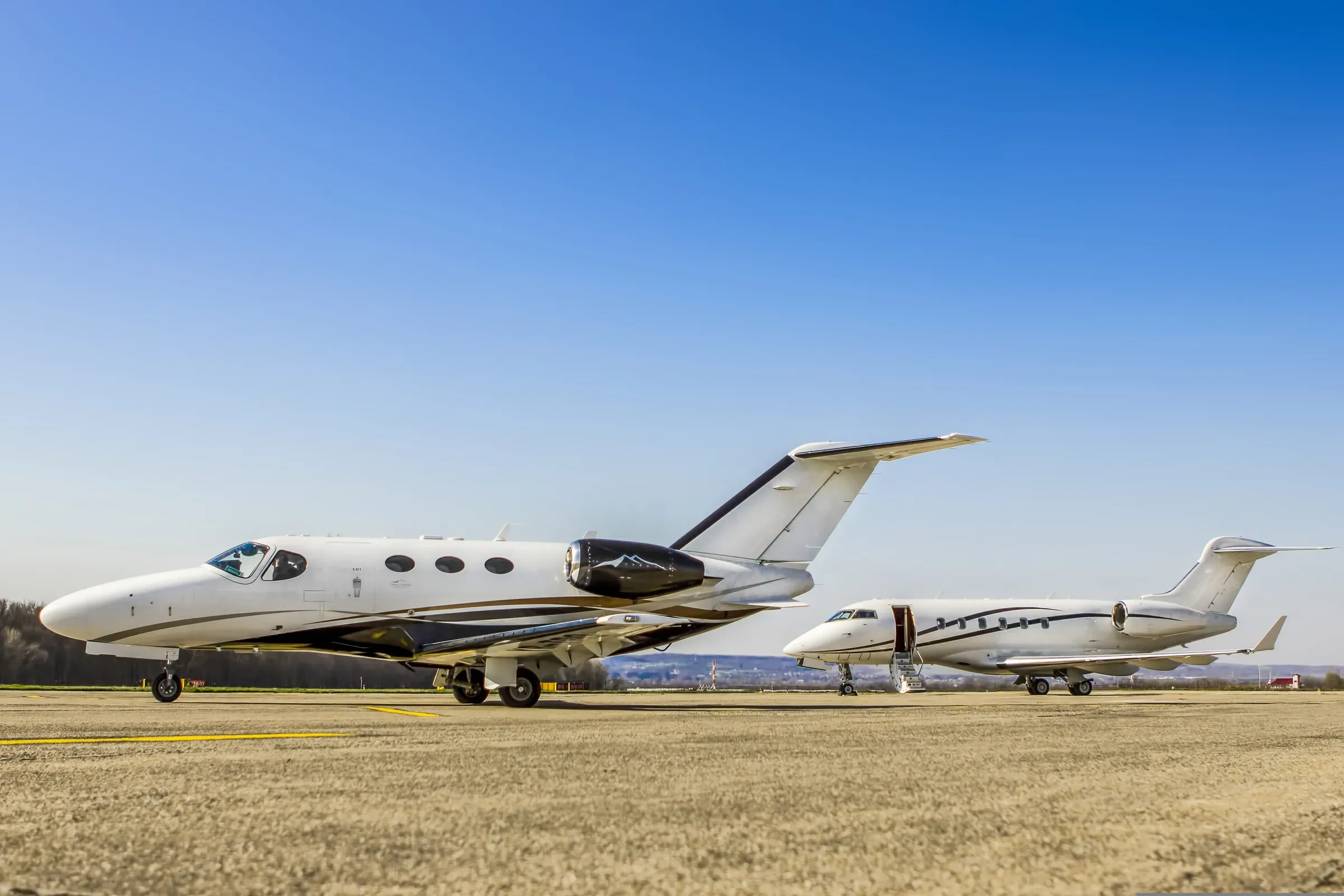 Two private jets parked on an airfield under a blue sky
