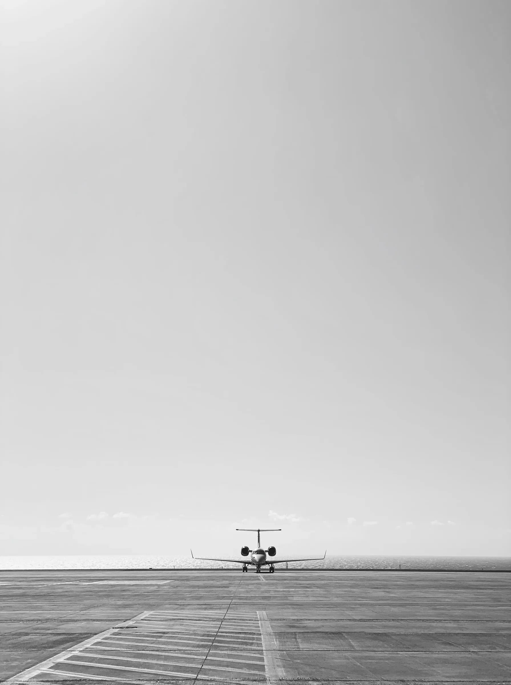 A private jet far off on an empty runway under a pale sky