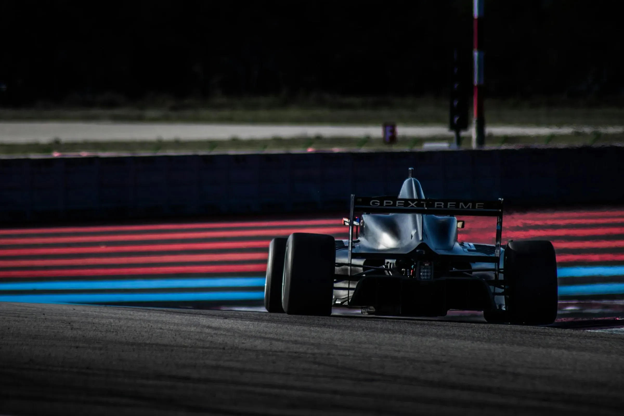 A single-seat race car on track at night beside striped kerbs