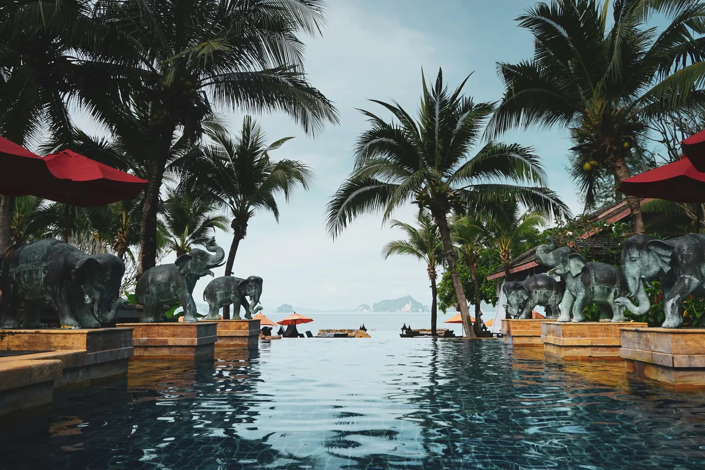 An infinity pool lined with stone elephants and palms, the sea beyond